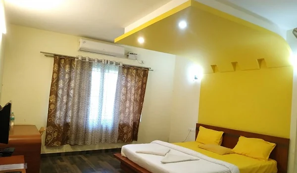 Deluxe air-conditioned room with yellow accent wall and TV at Narasinha Mehta Dham